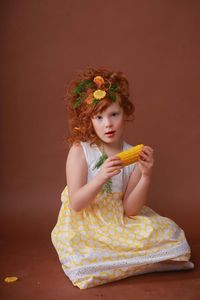 Portrait of girl holding corn against brown background