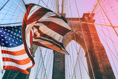 Low angle view of american flag against brooklyn bridge during sunset
