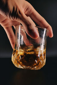 Cropped hand of woman holding drink against black background