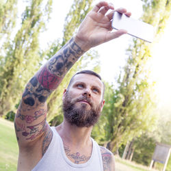 Man taking selfie on mobile phone against trees