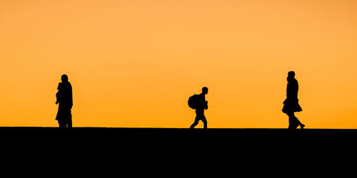 Silhouette people walking against clear sky during sunset