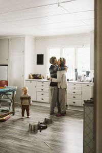 Loving lesbian couple kissing each other while standing by daughter in kitchen at home