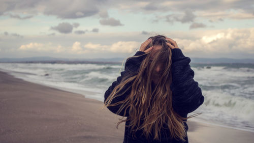 Rear view of woman standing at beach against sky