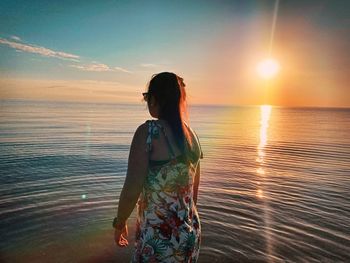 Woman looking at sea against sky during sunset