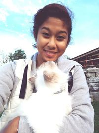 Portrait of smiling woman with dog sitting against sky