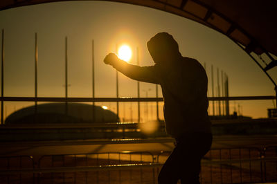 Low angle view of silhouette man standing by railing against sky during sunset