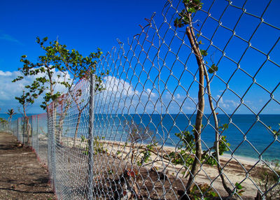 Fence by sea against clear blue sky