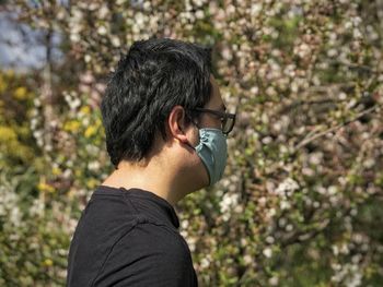Side view of man wearing glasses and face mask against flowering plants.