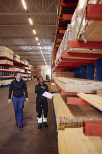 Full length of multiracial female workers examining planks on rack in lumber industry