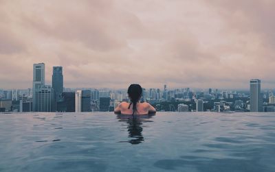 Rear view of man in swimming pool against buildings in city