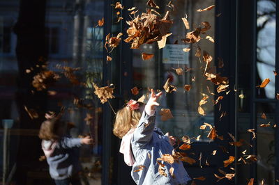 Girl throwing dry leaves in mid-air at city