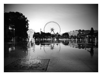 Fountains by ferris wheel in city against clear sky