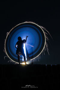 Low angle view of silhouette man standing against illuminated sky at night