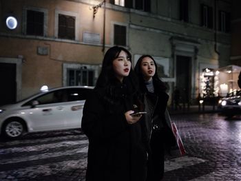 Young woman standing by car on street at night