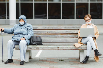 Portrait of business woman with laptop sitting on the bench with old woman in mask, social distance