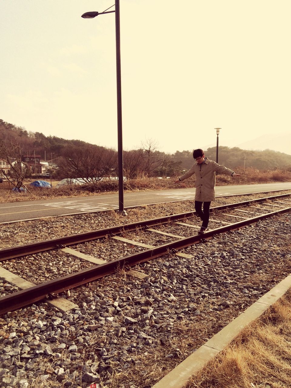 railroad track, full length, lifestyles, clear sky, transportation, rail transportation, standing, casual clothing, sky, leisure activity, rear view, walking, day, sunlight, outdoors, men, road, landscape