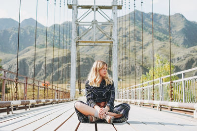 Woman sitting on footbridge against mountain