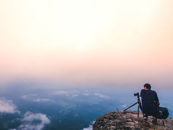 Rear view of man photographing on rock against sky during sunset