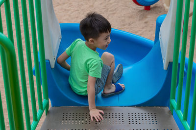 High angle view of boy sitting on slide in playground