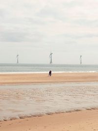 Distant view of mother and daughter at beach against sky