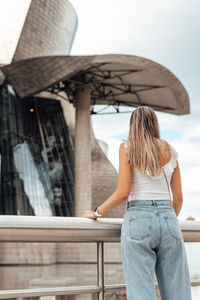 Rear view of woman standing by railing against building