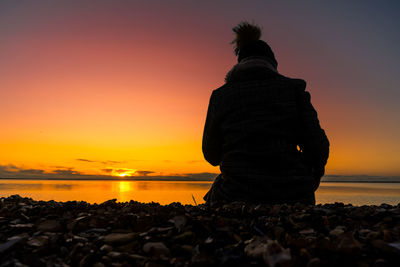 Rear view of rock on beach against sky during sunset