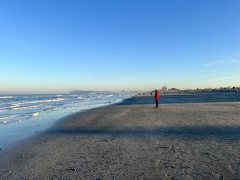 Rear view of woman walking at beach against clear blue sky