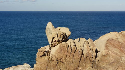 Scenic view of rocks by sea against sky