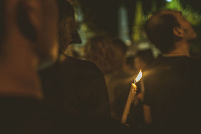 Woman holding lit candle while standing amidst people at night