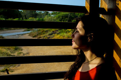 Side view of young woman looking out through window