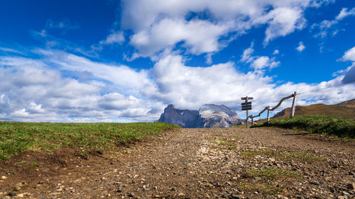 Dirt road amidst field against sky