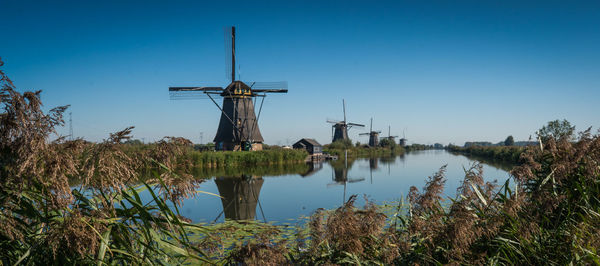 Traditional windmill by lake against clear blue sky