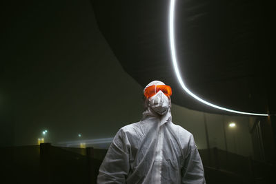 Rear view of man standing against illuminated light at night