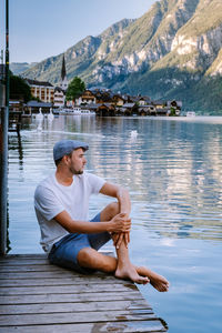 Young man sitting on lake against mountains