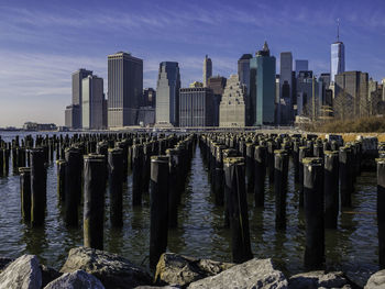 Wooden posts in sea in front of brooklyn cityscape
