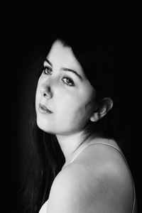 Close-up portrait of young woman against black background