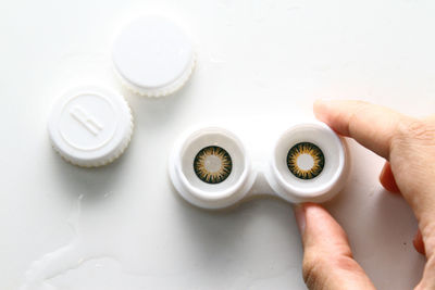 Close-up of hand holding contact lens against white background