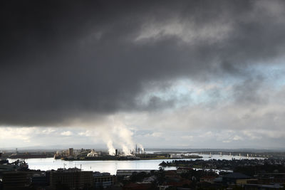 Smoke emitting from factory against cloudy sky