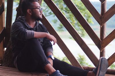 Young man looking away while sitting by railing