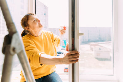 50 year old woman cleans windows from stains using rag and spray cleaner. 