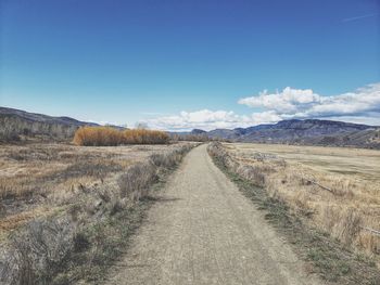 Dirt road amidst field against blue sky