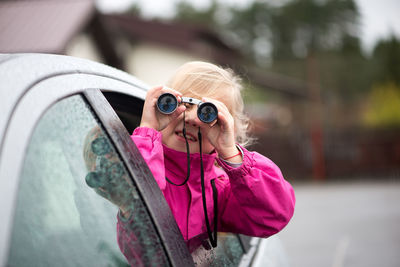 Sid view of girl looking through binoculars while traveling in car