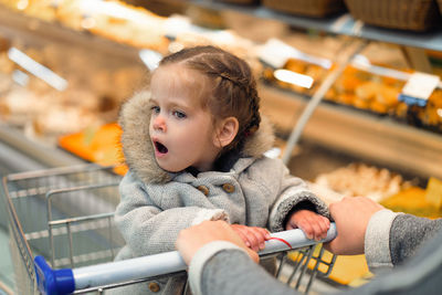 Girl sitting on shopping cart at supermarket