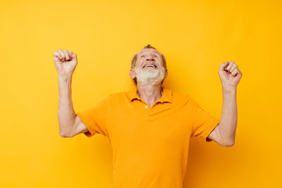 Portrait of woman with arms raised against yellow background