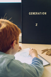 Rear view of boy writing on table