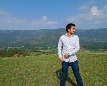 Portrait of young man standing on field against sky