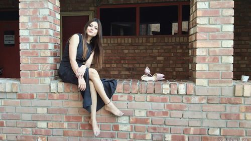 Portrait of young woman sitting on brick wall