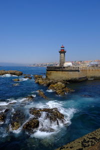 Lighthouse by sea against clear sky