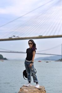 Full length of young woman standing on rock against sea