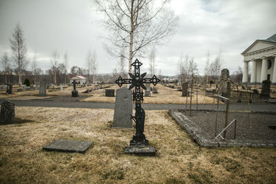 Bare trees in cemetery against sky